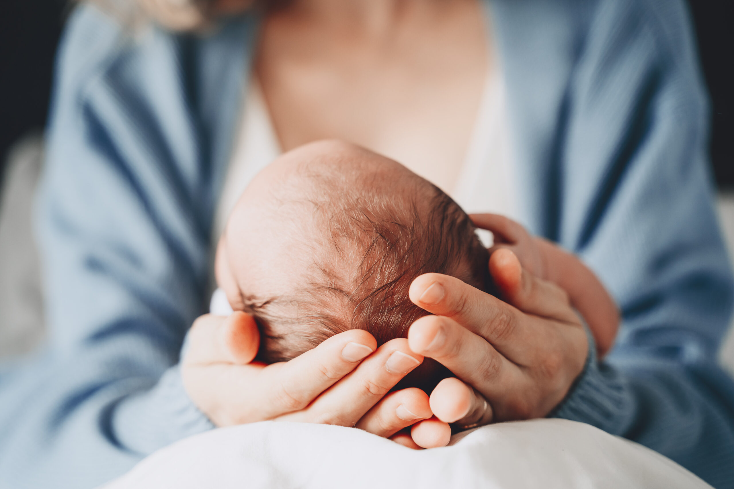A mother gently holding an infant's head in her hands. Mothers, we can help you with postpartum OCD in American Fork, UT. Let our ERP therapy be your guide!