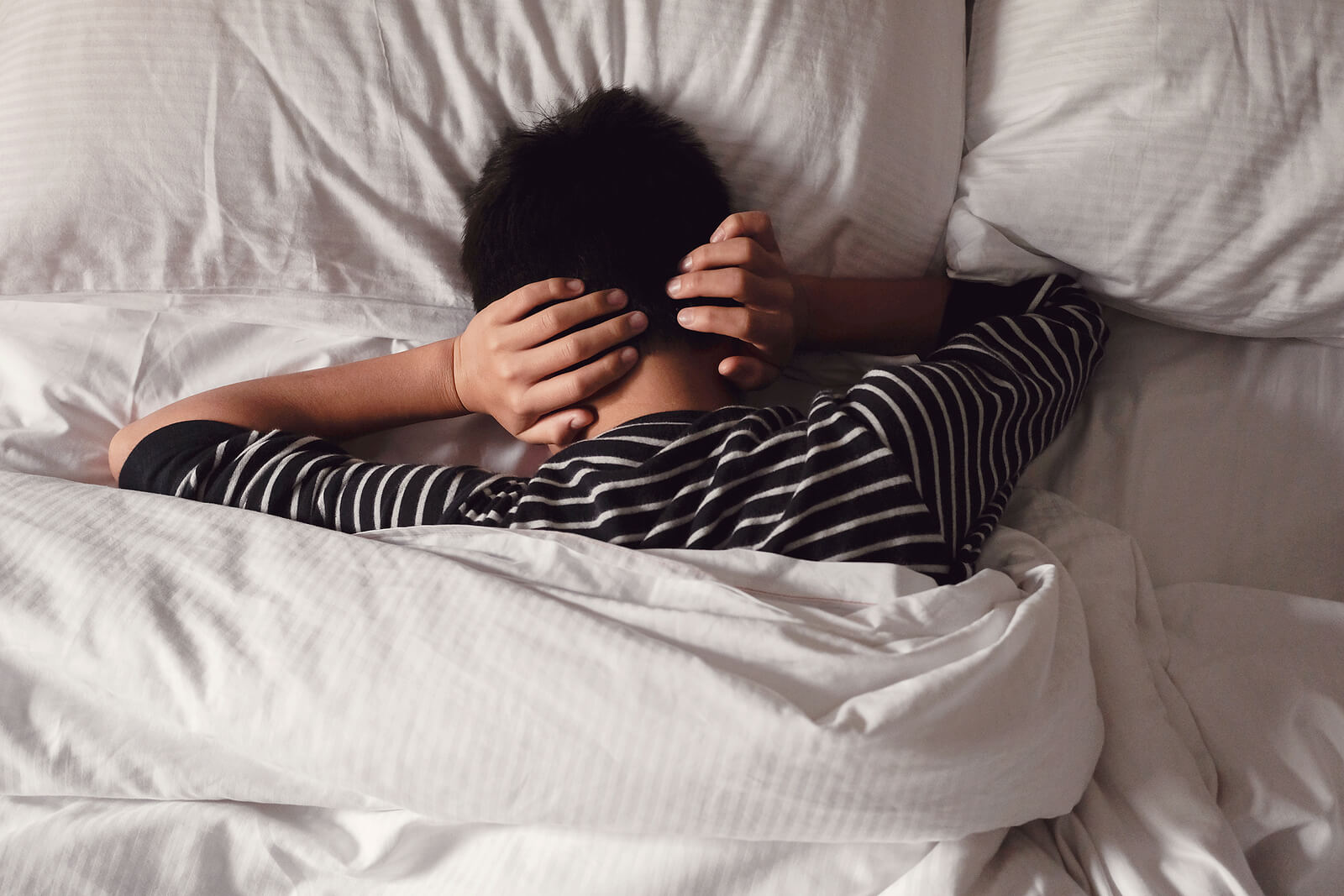 A young adult covering their ears while laying face down in their bed. Teen depression therapy in American Fork, UT can be the support your teen needs. Contact our depression therapists here.
