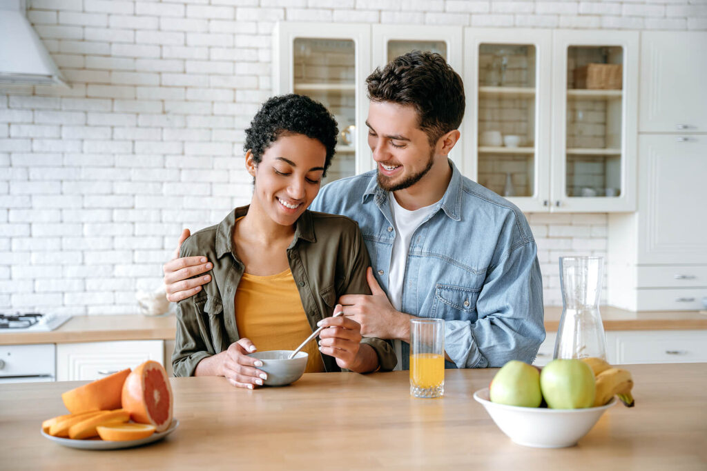 A biracial couple smiling at a table sharing fruit. With effective communication skills, your relationship can thrive. Learn more in marriage counseling in American Fork, UT.