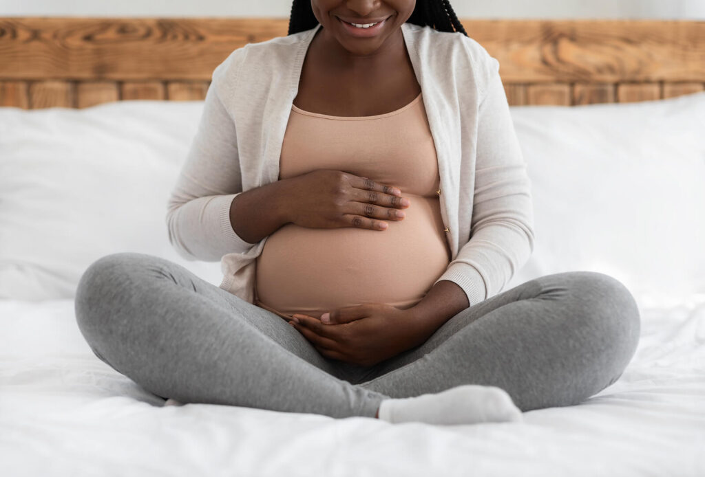 A woman holding her pregnant belly while sitting on a bed. Contact us today to begin ERP therapy in American Fork, UT for postpartum OCD. If you're a mother who has postpartum OCD, an ERP therapist is ready to help!