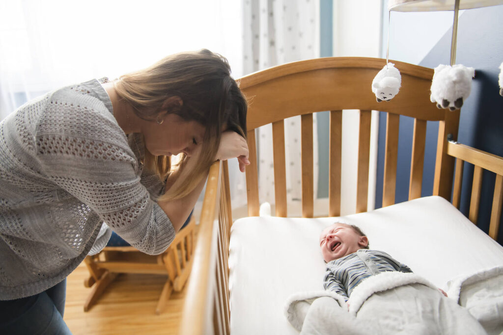 A mother feeling defeated while her infant cries in a crib. ERP therapy in American Fork, UT can help mothers enjoy motherhood again. Call today to learn more about how to treat postpartum OCD. 