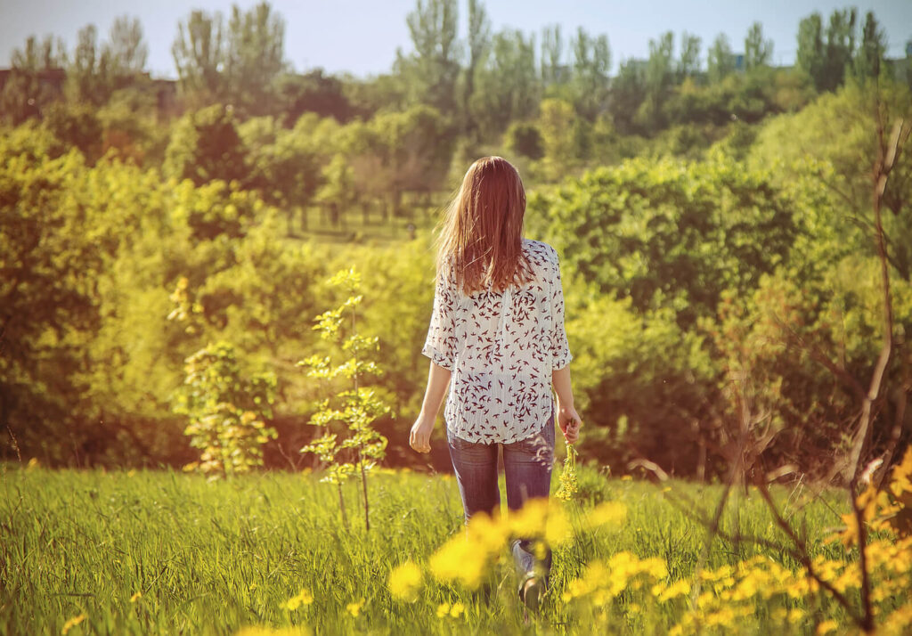 A woman walking away into a field of wildflowers. With faith deconstruction counseling, you can heal from past religious trauma. Learn more from a faith transition therapist in American Fork, UT.