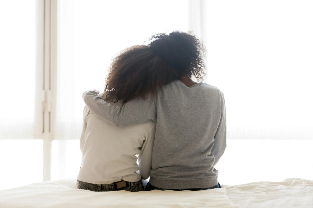 A mothers hugs their teen while sitting on the end of a bed and facing away from the camera. This could represent the bonds cultivated after working through therapy for teens in American Fork, UT. Learn how therapists for teens American Fork, UT can offer support by searching for therapy for teenage depression near me.
