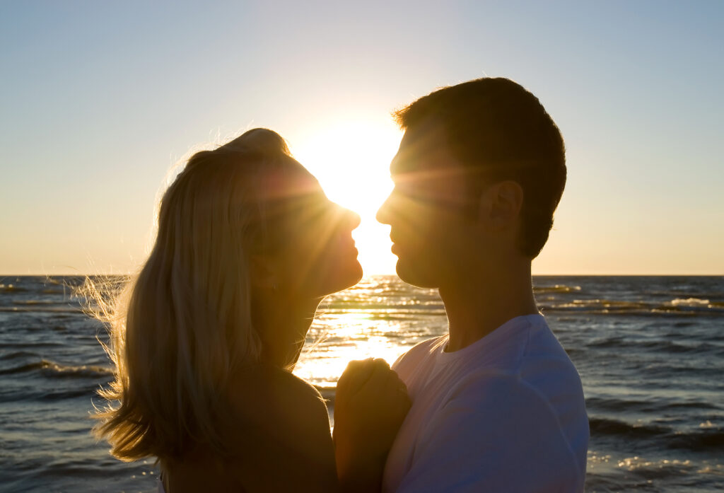 A couple stand face to face with loving expressions as the sun sets over the ocean. This could represent the bonds cultivated after working with a a therapist for couples American Fork, UT. Learn more about couples therapy in American Fork, UT and the help that "marriage counseling American, UT" can offer.
