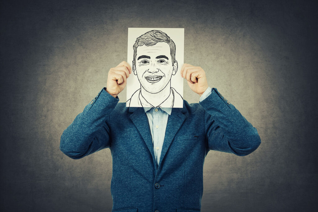 A person holds a paper with a drawn smiling face over their own face. This could represent hiding emotions as part of high functioning anxiety. Learn more about how a therapist American Fork can help by searching for anxiety treatment in American Fork, UT today.
