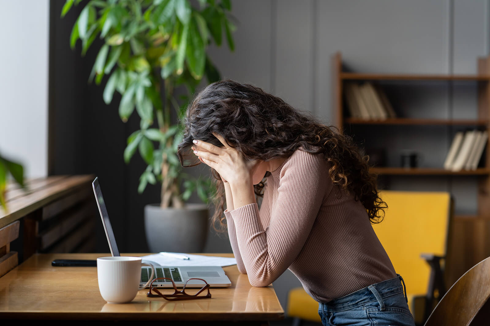 A woman touches her head while sitting at a computer desk. This could represent the stress of high functioning anxiety that anxiety treatment in American Fork, UT can help address. Learn more about anxiety counseling American Fork, UT by contacting an anxiety therapist American Fork, UT today.