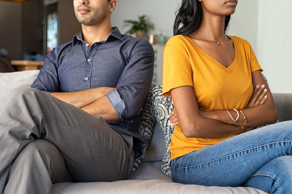 A couple sit on a couch while crossing their arms and facing away from one another. This could represent a relationship issue that couples counseling in American Fork, UT can help address. Learn more about couples therapy and how a couples therapist can offer support via couples communication therapy and other services. 
