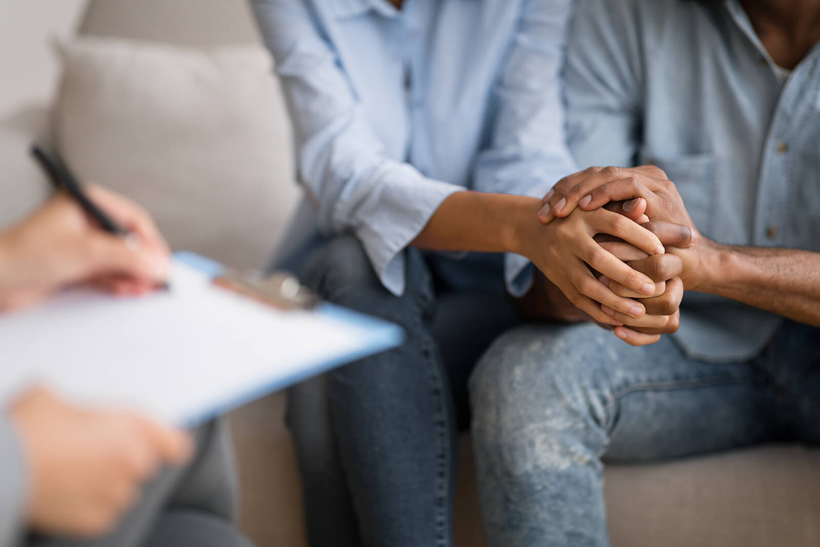 A close up of a couple holding hands while sitting across from a person with a clipboard. This could represent the support couples therapy for communication American Fork, UT can offer. Learn more about how a couples therapist can offer support by searching for couples counseling in American Fork, UT today.