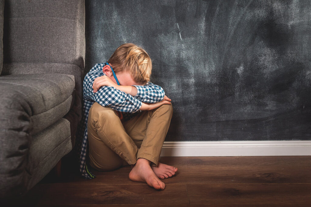 A child hides their face while appearing to cry against a wall and couch. This could represent the stress of depression that depression therapists in American Fork, UT can help address in different times of life. Learn more about signs of depression American Fork UT and how therapy for depression in American Fork, UT can help.
