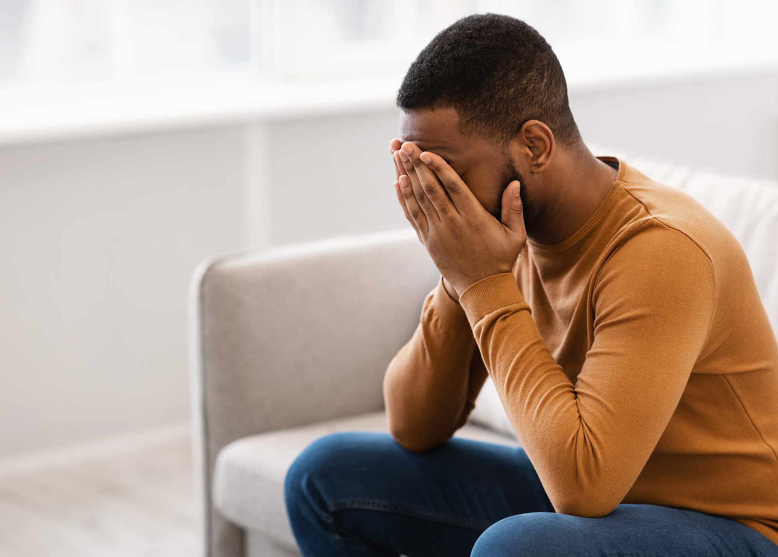 A man covers his face while sitting on a couch. learn how a therapist american fork can help address mental health concerns. Search for depression counseling in American Fork, UT and how an anxiety therapist American Fork, UT can help today.