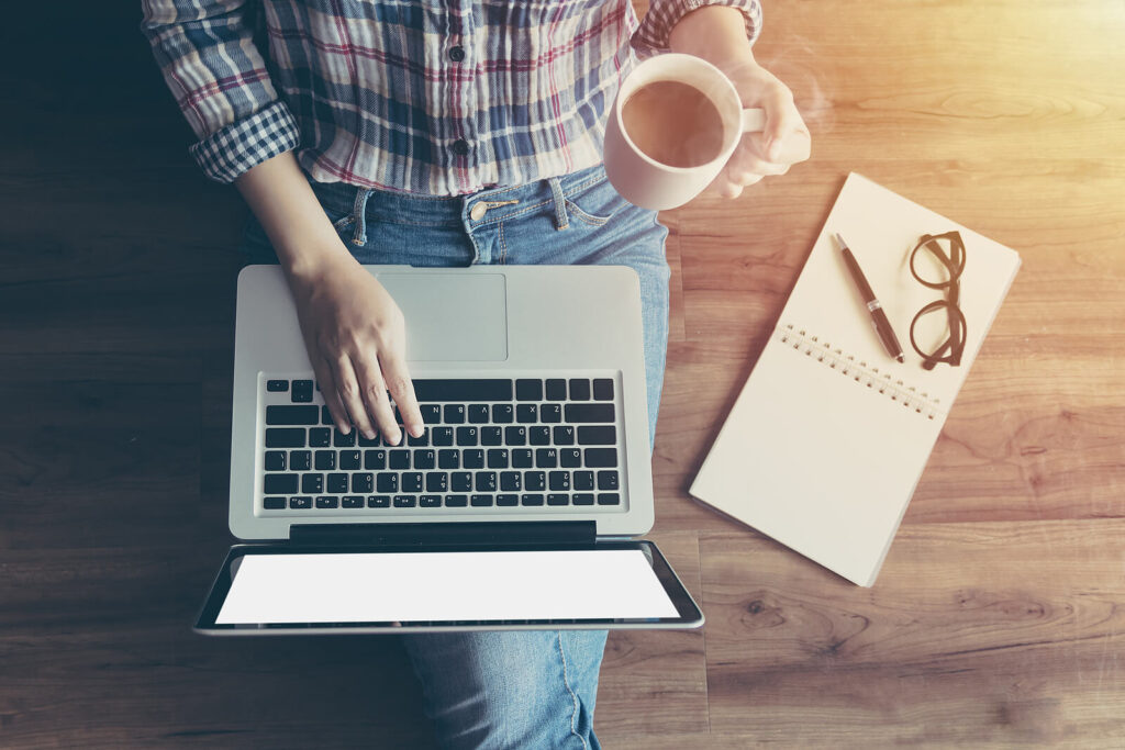 A top down view of a person holding a cup in one hand while typing on a laptop with a notepad nearby. Contact a therapist American Fork to learn more about the support that depression counseling or family therapy in American Fork, UT can offer. They can help you support loved ones through mental health crisis. 
