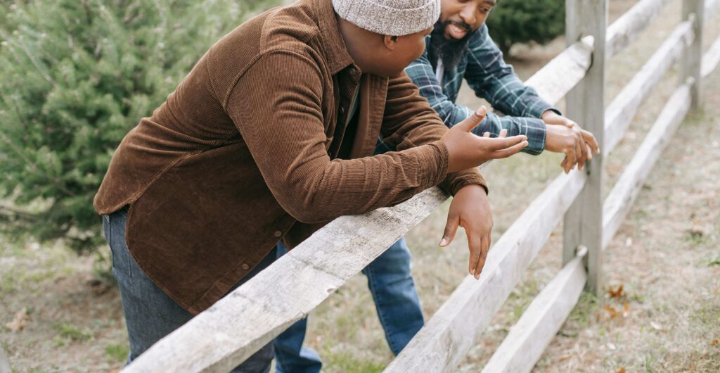 Two men lean on a wooden fence outdoors, engaged in a meaningful conversation. This could represent a father and son connecting with one another. Learn more about therapy for teens in American Fork, UT and how teenage counseling Utah can offer support. 
