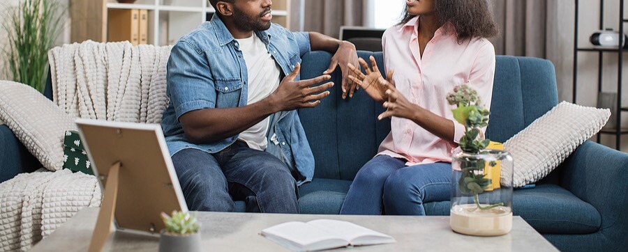 A couple sitting on a couch in conversation, with expressive gestures suggesting a discussion or disagreement. Search for how a marriage counselor in American Fork, UT can offer support for couples experiencing disagreements. Learn more about marriage counseling American Fork, UT and how couples therapy for communication American Fork, UT can help. 
