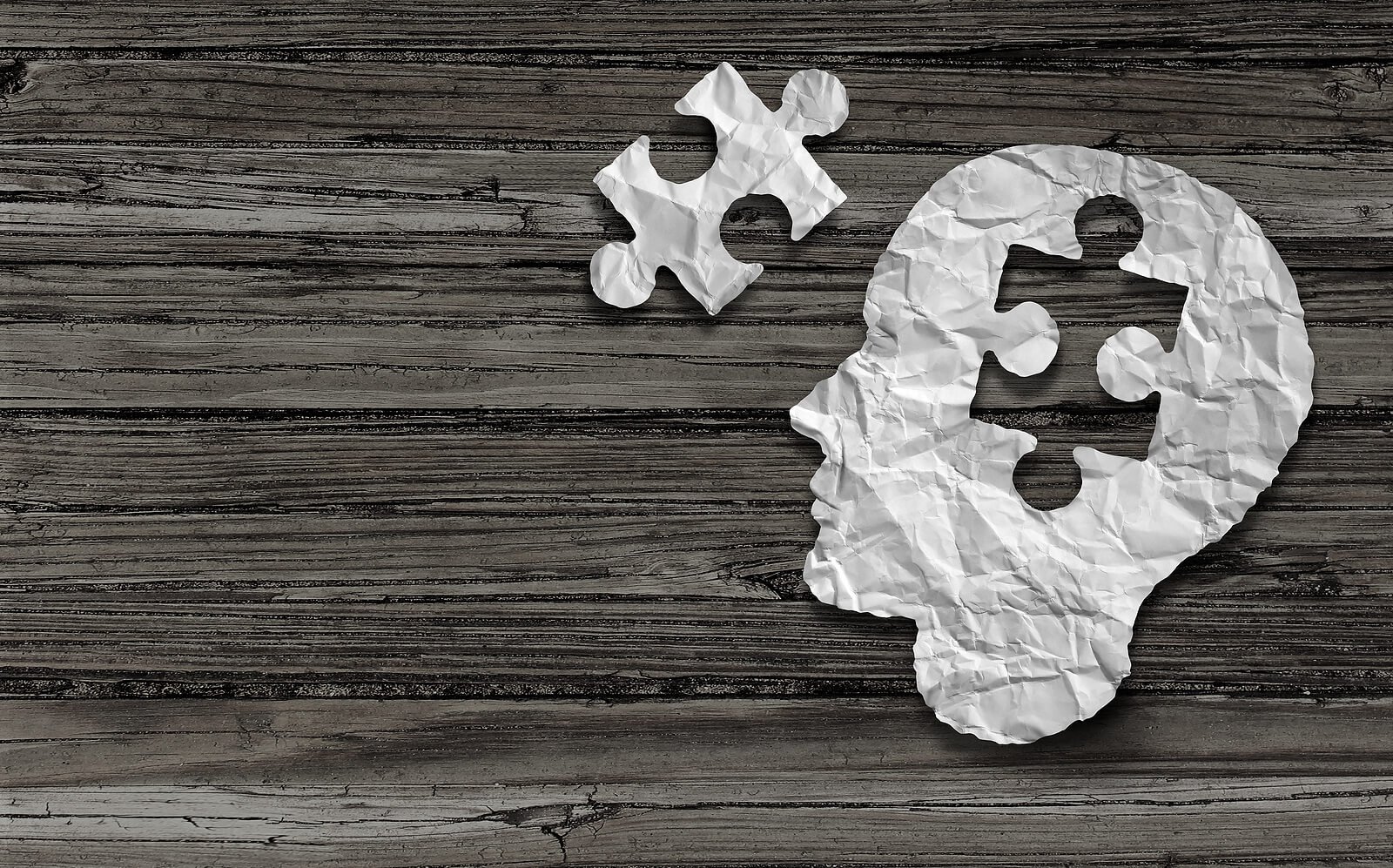 A crumpled paper cutout in the shape of a human head is placed on a wooden background. A missing puzzle piece hovers above the head, symbolizing a missing peace for mental healing that a trauma therapist in American Fork, UT can provide. Search for trauma therapy in American Fork, UT to learn more about attachment trauma in American Fork, UT today.